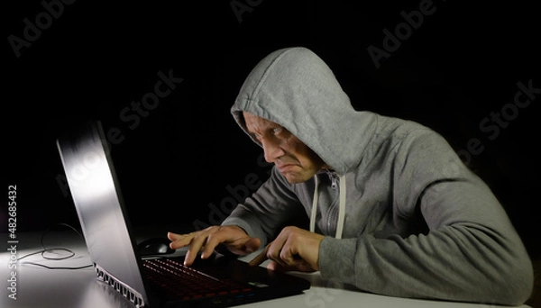 Obraz Computer scammer in the dark hacks personal data. Cybercriminal and computer, on a dark background.
