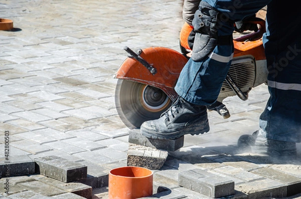 Fototapeta A worker cuts paving slabs with a gas cutter and a hand saw