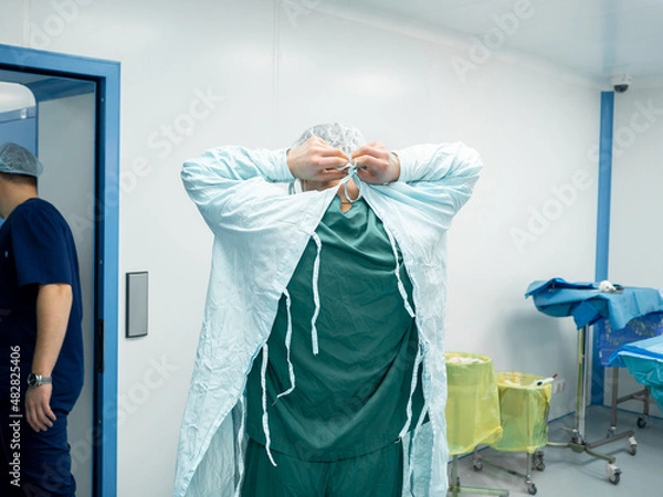 Fototapeta Rear view of the surgeon in the operating room removing the sterile operating gown at the end of the surgery. The surgeon undresses after surgery.