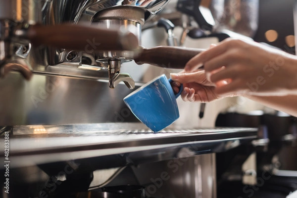 Obraz Cropped view of barista holding cup near portafilter of coffee machine in cafe.
