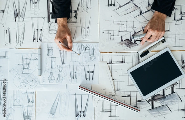 Fototapeta Table Top View of Designer Hands Drawing Blueprint Design on a Table with Digital Tablet and Sketches at Design Studio