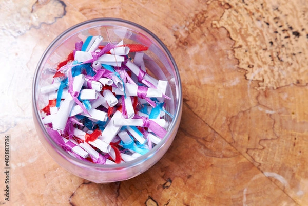 Fototapeta Paper notes with wishes tied with colored ribbons in a glass jar on a table on a wooden background. Wishes, congratulations, predictions concept. Copy space.