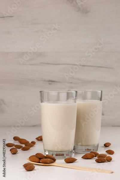 Fototapeta Two glasses with alternative dairy free almond milk and nuts on light background. Lactose free beverage