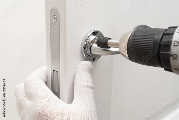 Fototapeta Man hands installing magnetic lock and door handle on  interior door using a screwdriver.