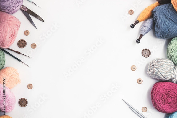 Fototapeta Panoramic view of composition with knitting accessories: balls of wool yarn, set of knitting needles, hooks, and other knit tools on white background. Long banner, top view, copy space, flat lay.