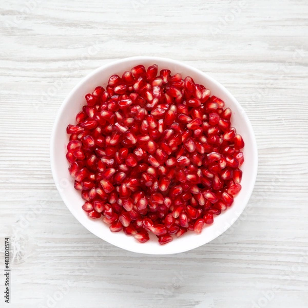 Fototapeta Red Pomegranate Seeds in a Bowl on a white wooden surface, top view. Flat lay, overhead, from above.