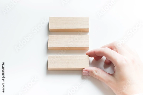 Fototapeta Blank three wooden blocks on a white background and a person's hand lays out the blocks