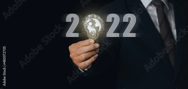 Fototapeta Businessman holding light bulb with virtual Global Internet connection 2022 and metaverse.