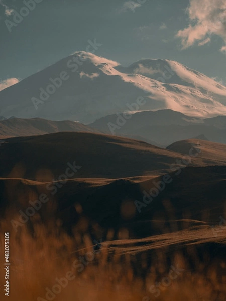 Fototapeta person sitting on the grass admiring the high snow-capped peak