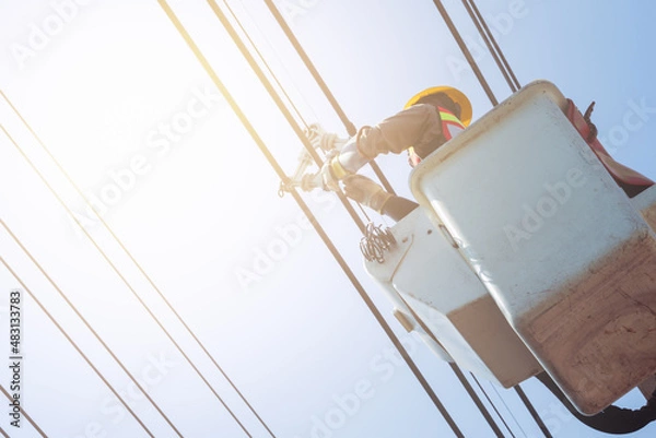 Fototapeta Electrical power line technicians perform maintenance on power lines by using a truck-mounted bucket.