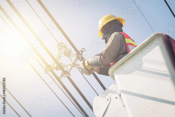 Fototapeta Electrical power line technicians perform maintenance on power lines by using a truck-mounted bucket.