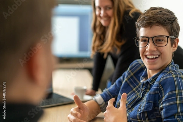 Fototapeta A young smiling intern in the office explains something to a colleague while a mentor in the background oversees the process