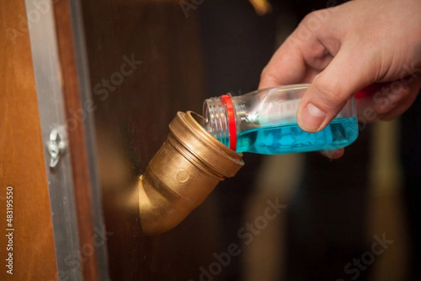 Obraz A man pours blue water from a bottle into a pipe.