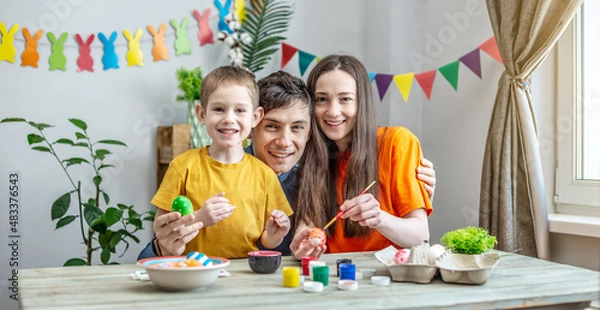 Obraz Family coloring Easter eggs in a decorated room. Mom, dad and child are having fun and preparing for the holiday
