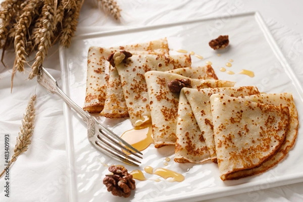 Fototapeta Homemade pancakes with walnuts and honey on a white fabric background. Pancake day.