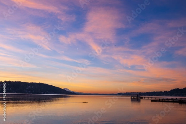 Fototapeta A colorful sky during sunrise with the moon in the sky, mountains in the background and a lake