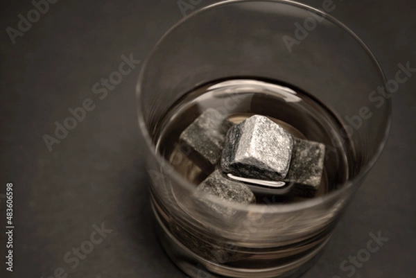 Fototapeta Gray whiskey soapstonestones in the glass. Close up view of whisky stones in the glass with whisky isolated on dark background whith copyspace