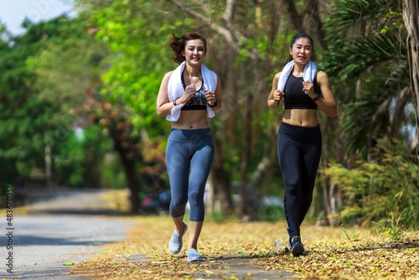 Fototapeta Two Asian woman running in the public park in the morning with warm light for sport, exercise and recreation concep