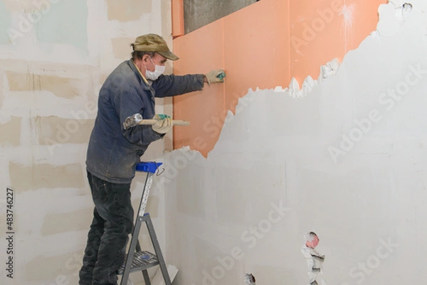 Fototapeta A worker on a stepladder breaks a wall of plaster blocks