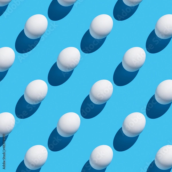 Fototapeta The pattern of their white eggs with a hard shadow on a blue background.