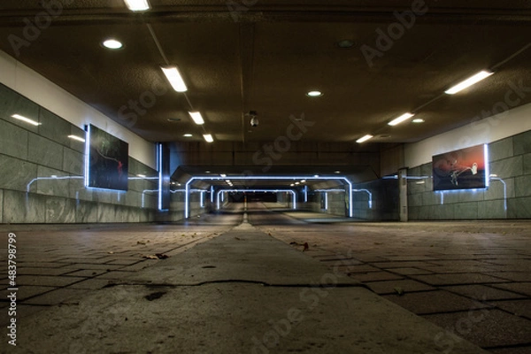 Fototapeta Picture of a modern underground building in the city. It is a tunnel for bikes and pedestrians. With lights above and on the sides, the lights reflecting in the walls. And paintings on the walls.