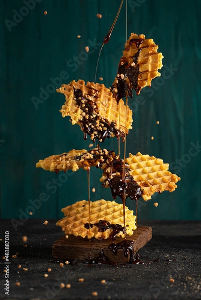 Fototapeta Flying thin round waffles with chocolate sauce and nuts, beautiful levitation or motion art photo. Homemade dessert. Copy space.