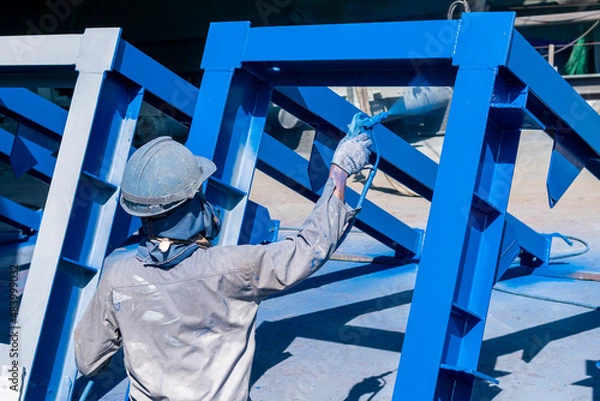Fototapeta The painter uses a spray gun to paint a steel structure before transportation to the assembly yard.
