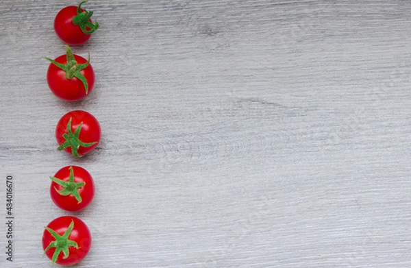 Fototapeta Small red tomatoes lie in a row on the left.