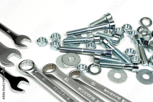 Obraz several silver color metal bolts with nuts and wrenches on a white background. close-up and copy space