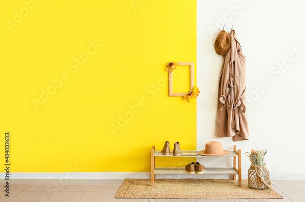 Fototapeta Stylish jacket and hat with frame hanging on color wall in hallway