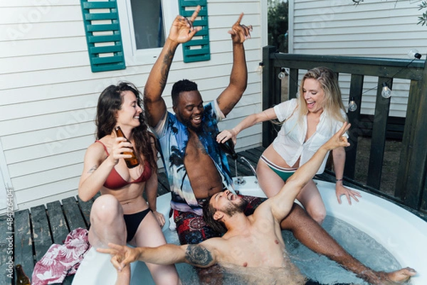 Fototapeta Four multiracial friends enjoying, laughing and drinking in a jacuzzi in summertime