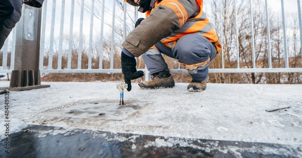 Fototapeta Road workers installing a new fence railing of bridge, outside the city 