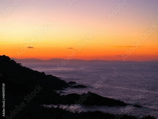 Fototapeta The rocks and the sea with the sunset in the background.