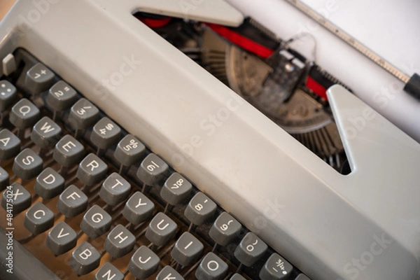 Fototapeta A Close Up Of A Mechanical Typewriter. The ribbon is tightly pressed against the white paper, waiting for the typist to choose which alphanumeric character is going to be imprinted on it next.