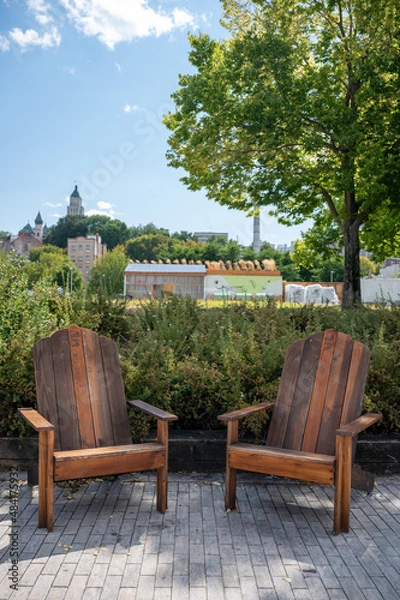 Fototapeta Two Wooden Outdoor Chairs Sit Empty Along The Boardwalk Beside The Marina In The Ports Area Of Quebec City.