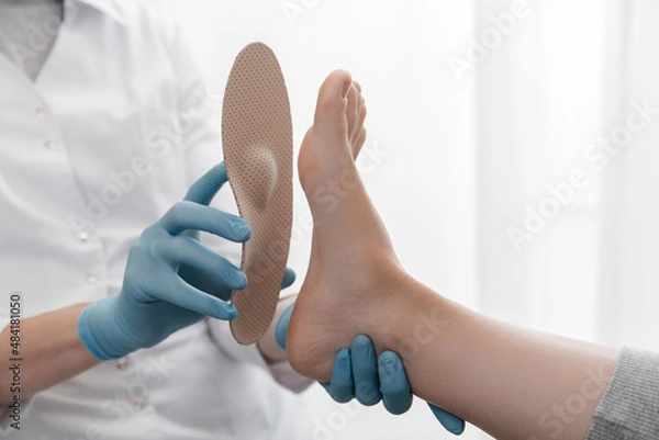 Fototapeta Orthopedic insole on a white background. Hands in rubber gloves hold an orthopedic insole. Foot care, comfort for the feet. Doctor orthopedist tests the medical device. Flat feet correction