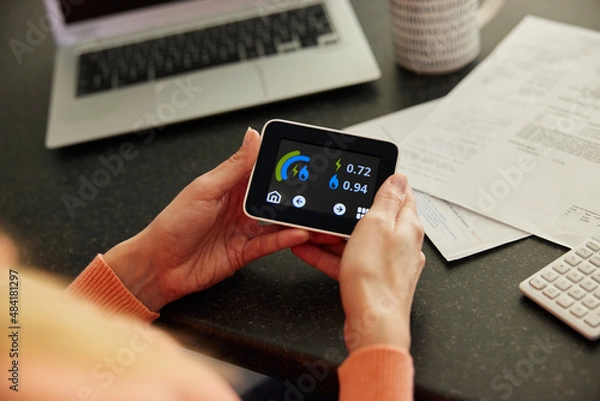 Obraz Close Up Of Woman Holding Smart Energy Meter In Kitchen Measuring Electricity And Gas Use With Bills With Calculator