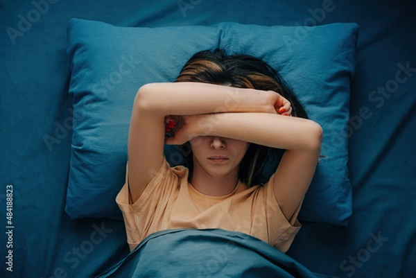 Obraz A woman with a headache or migraine lies in bed. Top view.