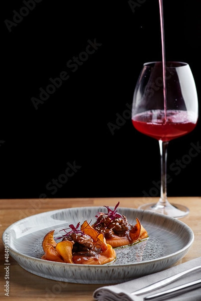 Fototapeta beef with sauce and sweet potato on a restaurant table with a glass of wine close up. restaurant dinner with dark background