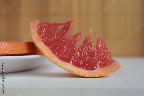 Fototapeta A red slice of grapefruit on a wooden table.