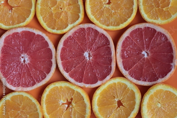 Obraz Citrus fruits cut into slices on an orange surface.	