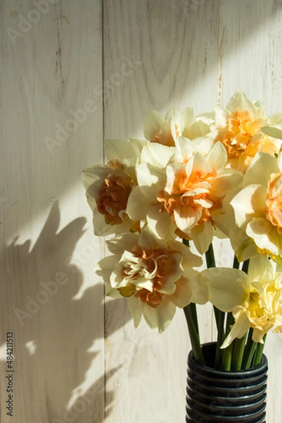 Fototapeta Bouquet of daffodils. Flowers on the background of a light wooden wall. Spring bouquet. Vertical. copy space.