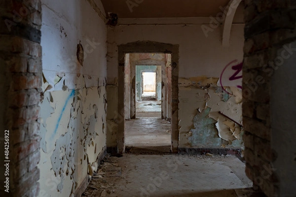Fototapeta Dark corridor in an abandoned public building next to the staircase. Urban exploration in an old horror house. Paint is peeling off the walls and dirt is lying on the floor. Doors have been removed.
