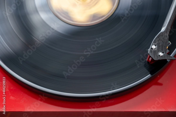 Fototapeta A Vinyl Spins On A Red Turntable With The Needle Head Visible.