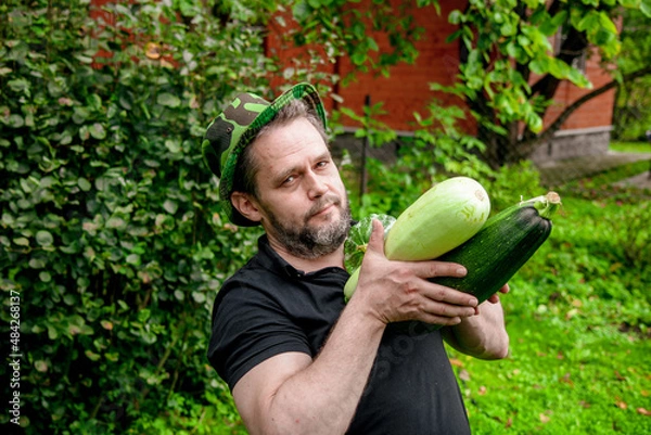 Fototapeta Portrait of a man harvesting organic vegetables.The gardener holds ripe, juicy zucchini in his hands	

