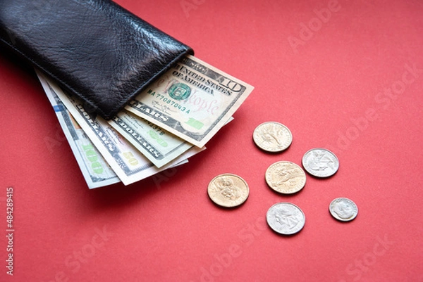 Fototapeta black leather wallet with dollar bills in different denominations and coins on a red background