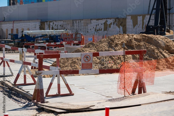 Obraz fenced area of the construction site. Red and white safety barriers enclose a pile of soil. There is warning sign on the barrier. Translation: "Danger area! Keep out!"