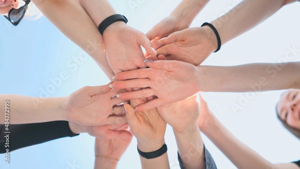 Fototapeta Cheerful girls join hands together as a sign of unity and joint successful work. Teamwork stacking hand concept.