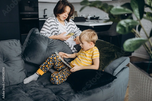 Obraz children at home, sitting on the couch, playing with gadgets