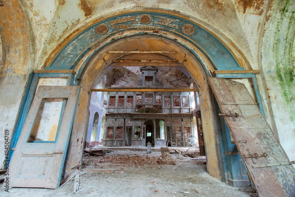 Fototapeta The ruined blue entrance with a semicircular arch to the middle part of the old destroyed and abandoned Orthodox church in Russia. The destroyed iconostasis is visible. Broken doors. Peeling paint and